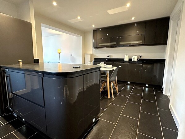 Een moderne keuken met donkere kastjes, een centraal eiland en een eetgedeelte met een tafel en stoelen.