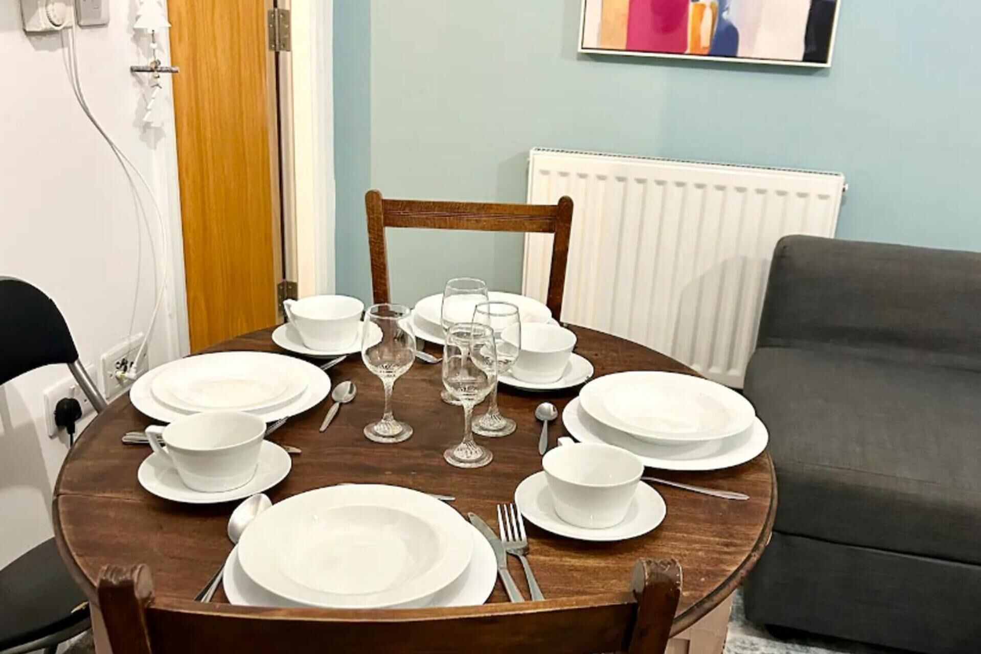 Mesa de jantar posta com pratos, tigelas e copos de vinho brancos, rodeada por cadeiras.