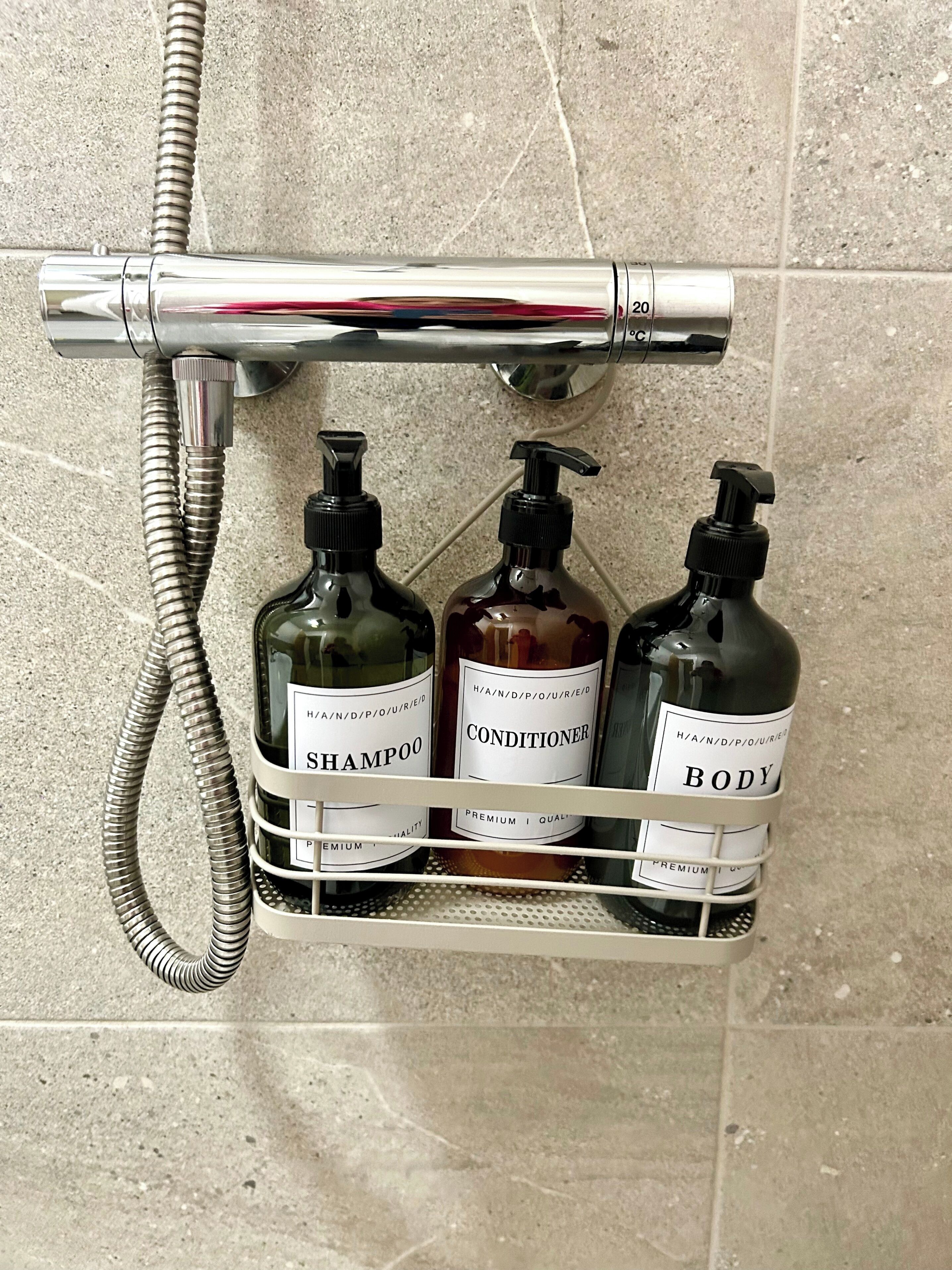 A shower area with a chrome faucet and a hose, and three bottles of shampoo, conditioner, and body wash in a metal rack.