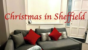 A modern living room with a grey sofa, red and grey cushions, and a rolled-up grey blanket on the floor.
