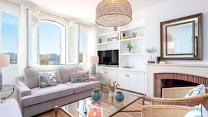 A modern living room with a sofa, coffee table, wicker chairs, a fireplace, and a large window with a city view. - Penthouse With Private Terrace Stunning Views Plaza de la Marina (Málaga)