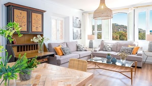 A modern living room with a sofa set, a dining table, and a large window offering a view of the hills. - Penthouse With Private Terrace Stunning Views Plaza de la Marina (Málaga)