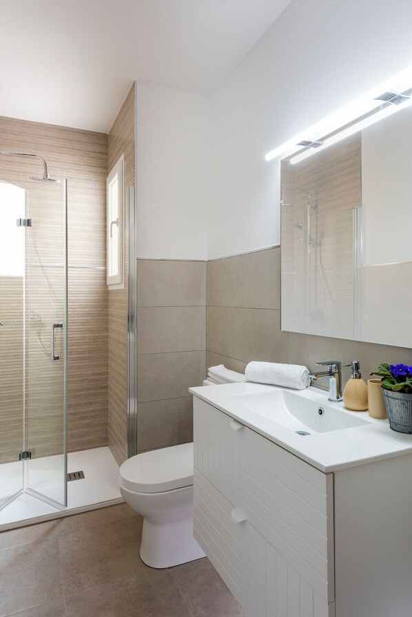 Un bagno moderno con cabina doccia in vetro, un water bianco e un mobile lavabo con specchio.