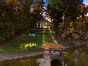 A lakeside property with a dock, a swimming pool, and a house with a well-maintained lawn and outdoor seating area. - Game Room, Covered Dock, Kayaks, Firepit, 2 Kings (Sherrills Ford)