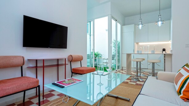 A modern living room with a glass coffee table, red upholstered chairs, a flat-screen TV, and a sofa with a striped cushion. - Private Terrace 5 min Walk to Cathedral 2Bd Apartment Galera II (Seville)