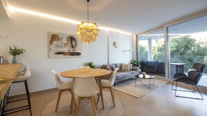 A modern living room with a round wooden table, white chairs, a sofa, and a large window offering a view of greenery. - Sea View Apartment Near The Beach (Fuengirola)