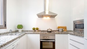 Une cuisine moderne avec des armoires blanches, des comptoirs en granit, une hotte de cuisinière en acier inoxydable, un four et un four à micro-ondes.