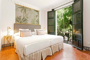 A bedroom with a large bed, a nightstand, a lamp, a painting, and a view of the outdoors. - Spectacular Apartment With 258m2 and 4BD Near Alcazar San Fernando (Seville)