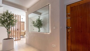 Un couloir avec un grand miroir, une porte en bois et des plantes en pot.