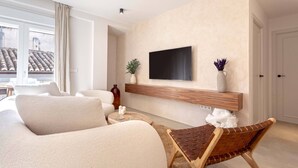 Un salon moderne avec un canapé, une table basse, un téléviseur fixé au mur et une étagère en bois en dessous.