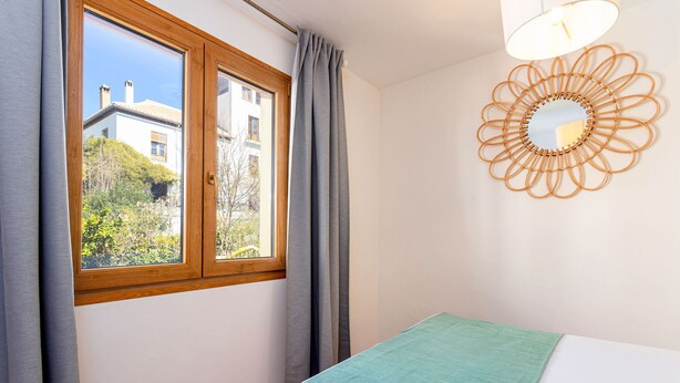 A bedroom with a window, a bed with a green blanket, and a wall-mounted mirror. - Stunning 4 Bedroom House in Albaicin Alhacaba (Granada)