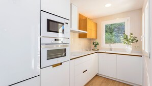 A kitchen with white cabinetry, a built-in oven, a microwave, and a window with a view of greenery. - Stunning 4 Bedroom House in Albaicin Alhacaba (Granada)