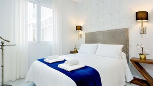 A hotel room with a large bed, two bedside lamps, a nightstand with a vase, and a window with curtains. - Spacious 3 Bd Apartment With Views to the Metropol Encarnacion (Seville)