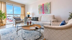 Un salon moderne comprenant un canapé, des fauteuils, une table basse et une grande fenêtre donnant sur la ville.