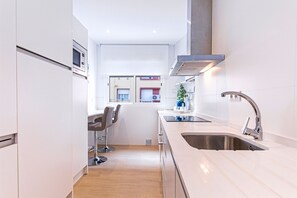 Une cuisine moderne avec un évier en acier inoxydable, un tabouret de bar et une fenêtre donnant sur un immeuble.