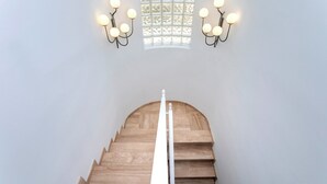A staircase with a wooden handrail and a white balustrade, leading to a room with a large window and wall-mounted sconces. - Spectacular House With Private Pool on the Beachfront Mirador de La Barrosa (Chiclana de la Frontera)