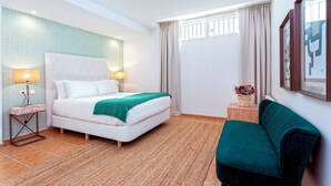 A hotel room with a bed, two bedside lamps, a green sofa, a window with curtains, and a wall-mounted picture. - Spectacular House With Private Pool on the Beachfront Mirador de La Barrosa (Chiclana de la Frontera)