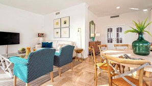 A modern living room with a sofa, two patterned chairs, a dining table with chairs, a TV, framed pictures on the wall, and a green vase on the table. - Spectacular House With Private Pool on the Beachfront Mirador de La Barrosa (Chiclana de la Frontera)