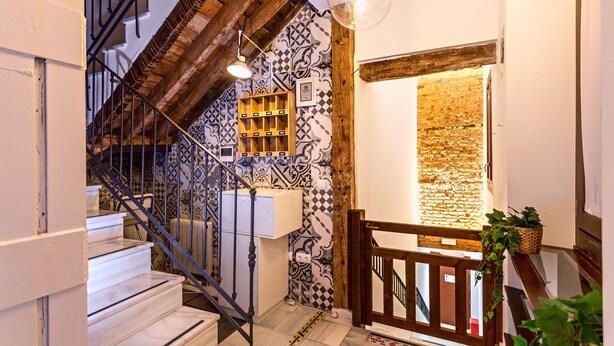 Una escalera con barandilla de madera, pared con diseño y lámpara colgante.