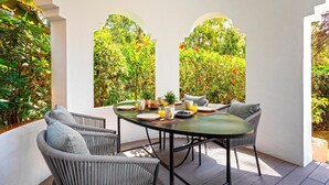 A covered outdoor dining area with a round table, wicker chairs, and a view of lush greenery through arched openings. - Spectacular Apartment With Pool and Direct Acces to the Beach Venalmar Terrace (Estepona)