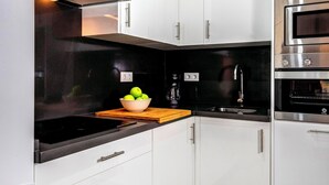 A modern kitchen with white cabinetry, a black countertop, a stainless steel range hood, a built-in oven, and a bowl of green apples. - Spacious Bright With Excellent Location 1 Bd Aptm Tomas de Ibarra (Seville)