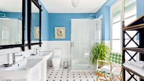 Une salle de bain avec un mur bleu, des carreaux blancs, une douche en verre, un lavabo blanc, des toilettes et une chaise à motifs verts et blancs.