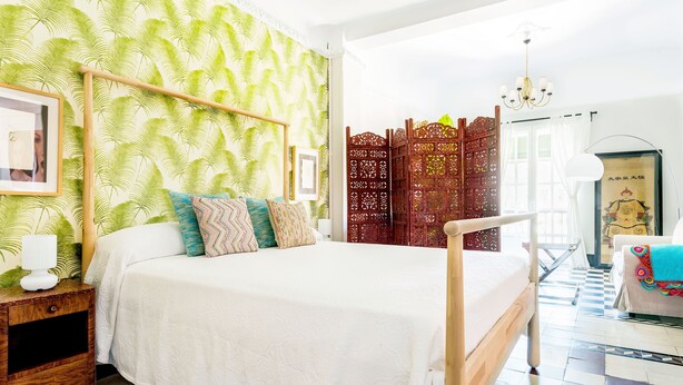 Une chambre à coucher comprenant un lit, une table de chevet, un paravent décoratif et une chaise.