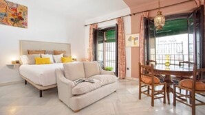Ein Schlafzimmer mit einem Bett, einem Sofa, einem Esstisch mit Stühlen und einem Fenster mit Vorhängen.
