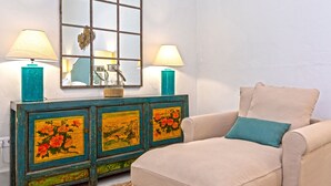 A room with a beige sofa, teal cushions, a wooden cabinet with floral paintings, and two lamps. - Unique Sevillian Palace-house in Santa Cruz Abades Terrace (Seville)