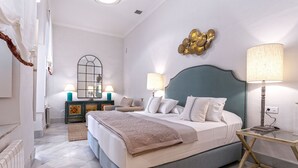 A bedroom with a bed, two bedside tables, a mirror, and a decorative wall piece. - Unique Sevillian Palace-house in Santa Cruz Abades Terrace (Seville)
