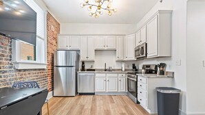 A modern kitchen with white cabinets, stainless steel appliances, and a wooden floor.