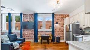 A modern living space with a brick wall, a sofa, a dining table, and a kitchen area.