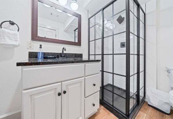 A bathroom with a glass shower enclosure, a sink with a marble countertop, and a mirror above the sink.