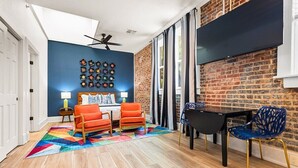A room with a brick wall, a ceiling fan, a TV, a table with chairs, and a colorful rug. - Stylish Loft Retreat in Downtown Hot Springs (Hot Springs)