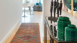 Un couloir avec un tapis à motifs, une table sur laquelle sont posés des bocaux verts et un tableau accroché au mur.