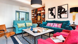 A modern living room with a blue sofa, a teal sofa, and a red armchair. There is a coffee table with books and a lamp. A bookshelf filled with books and decorative items is visible. - Wonderful Apartment 200m2 - 4 Bedrooms - 3 Bathrooms in the Best Location Albareda (Seville)