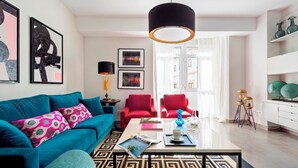 A modern living room with a teal sofa, red chairs, a coffee table, and artwork on the walls. - Wonderful Apartment 200m2 - 4 Bedrooms - 3 Bathrooms in the Best Location Albareda (Seville)