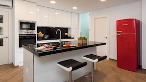 Eine moderne Küche mit weißen Schränken, einer schwarzen Arbeitsplatte, einem roten Kühlschrank und zwei Barhocker.