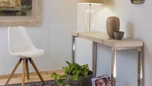 Ein modernes Wohnzimmer mit einem weißen Sessel, einer Lampe, einem Konsolentisch mit Dekoration und einem gerahmten Gemälde an der Wand.