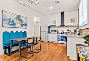 A modern kitchen with a dining area, white cabinetry, a stainless steel refrigerator, and a microwave.
