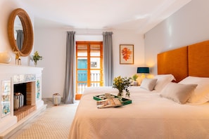 Habitación de hotel con chimenea, una cama con sábanas blancas, una mesita de noche con lámpara y una ventana con cortinas.