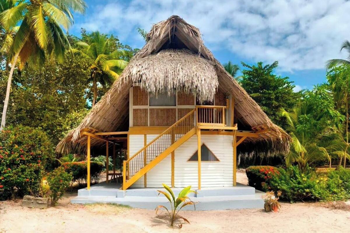 A thatched-roof bungalow with a wooden balcony and a staircase leading to the entrance.