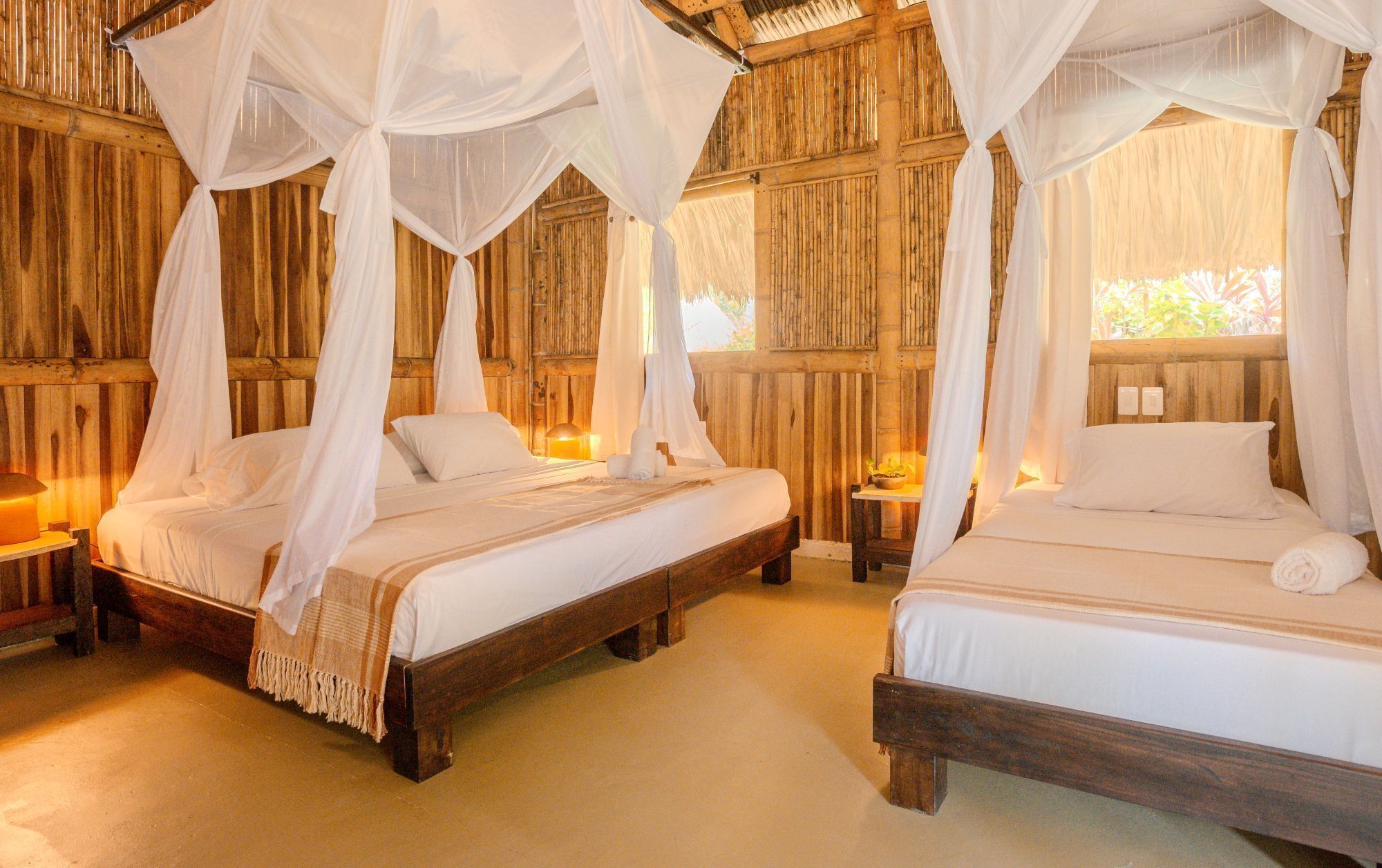 Dos camas de madera con ropa blanca y dosel, en una habitación con paredes de madera y un ambiente cálido.