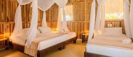 Two wooden beds with white bedding and canopy beds, in a room with wooden walls and a warm ambiance.