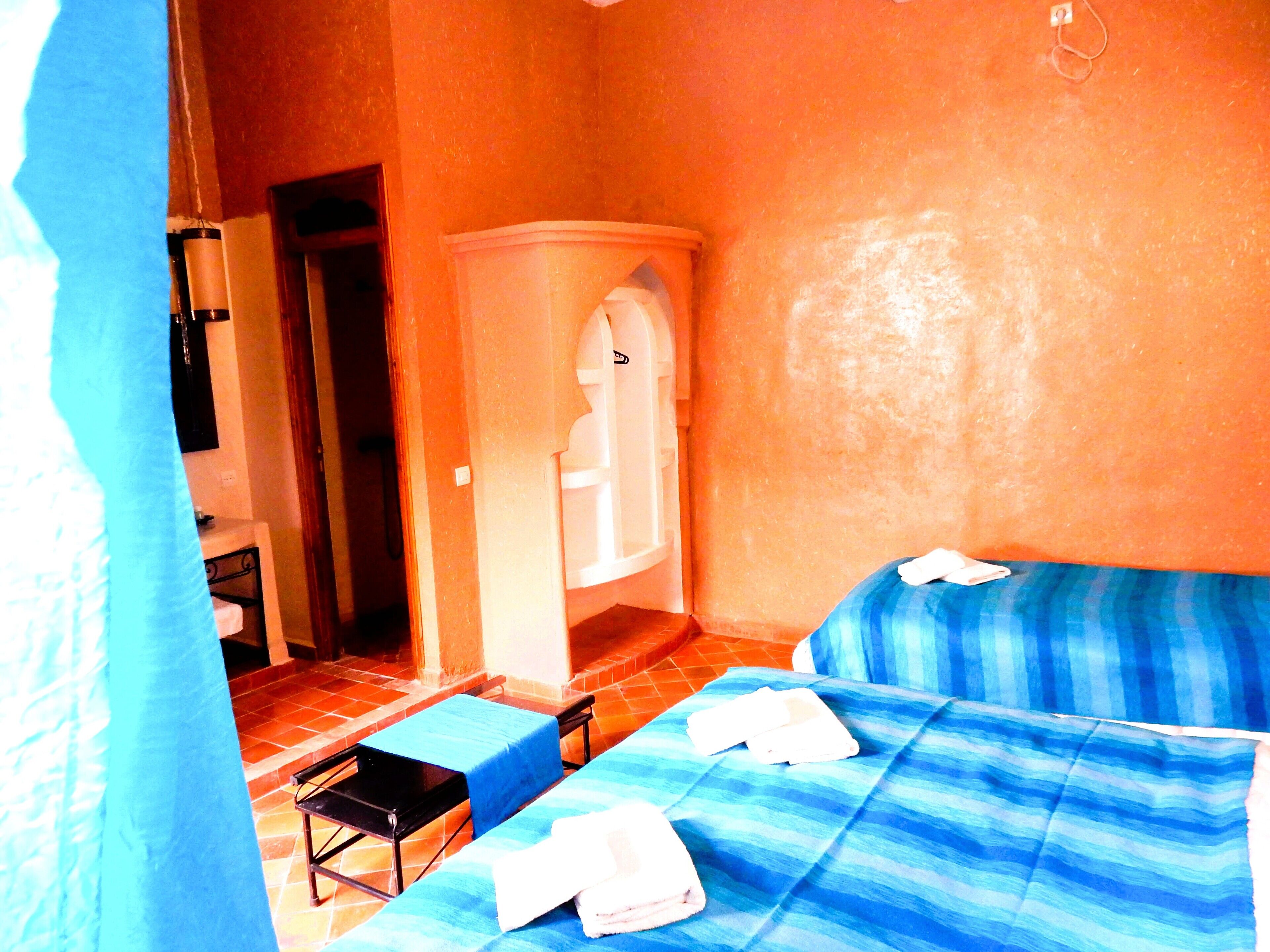 A room with two beds, a small table, and a shower area.
