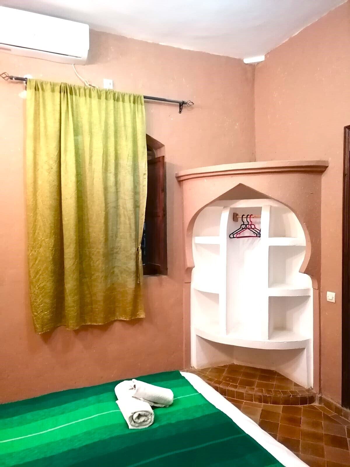 A small room with a green-striped bed, a white shelf unit, and a green curtain.