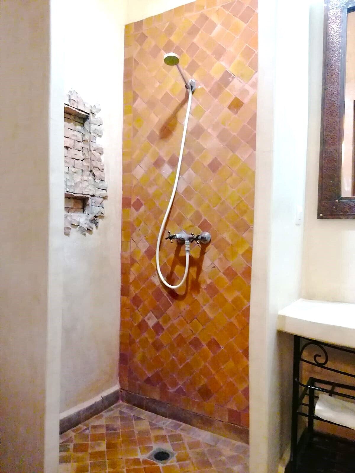 Une douche avec un mur recouvert de mosaïques et un petit élément décoratif en briques.
