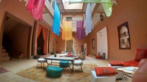 A spacious room with a high ceiling, a central table, and a seating area with ottomans. - Riad Tazawa (Ait Sedrate Sahl El Gharbia)