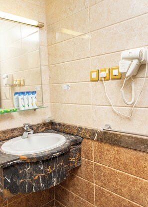 A bathroom with a marble sink, a hairdryer, and toiletries on a shelf.