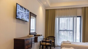 A hotel room with a bed, a desk with a mirror, a chair, and a television on the wall. - Dufla Hotel  (Makkah)
